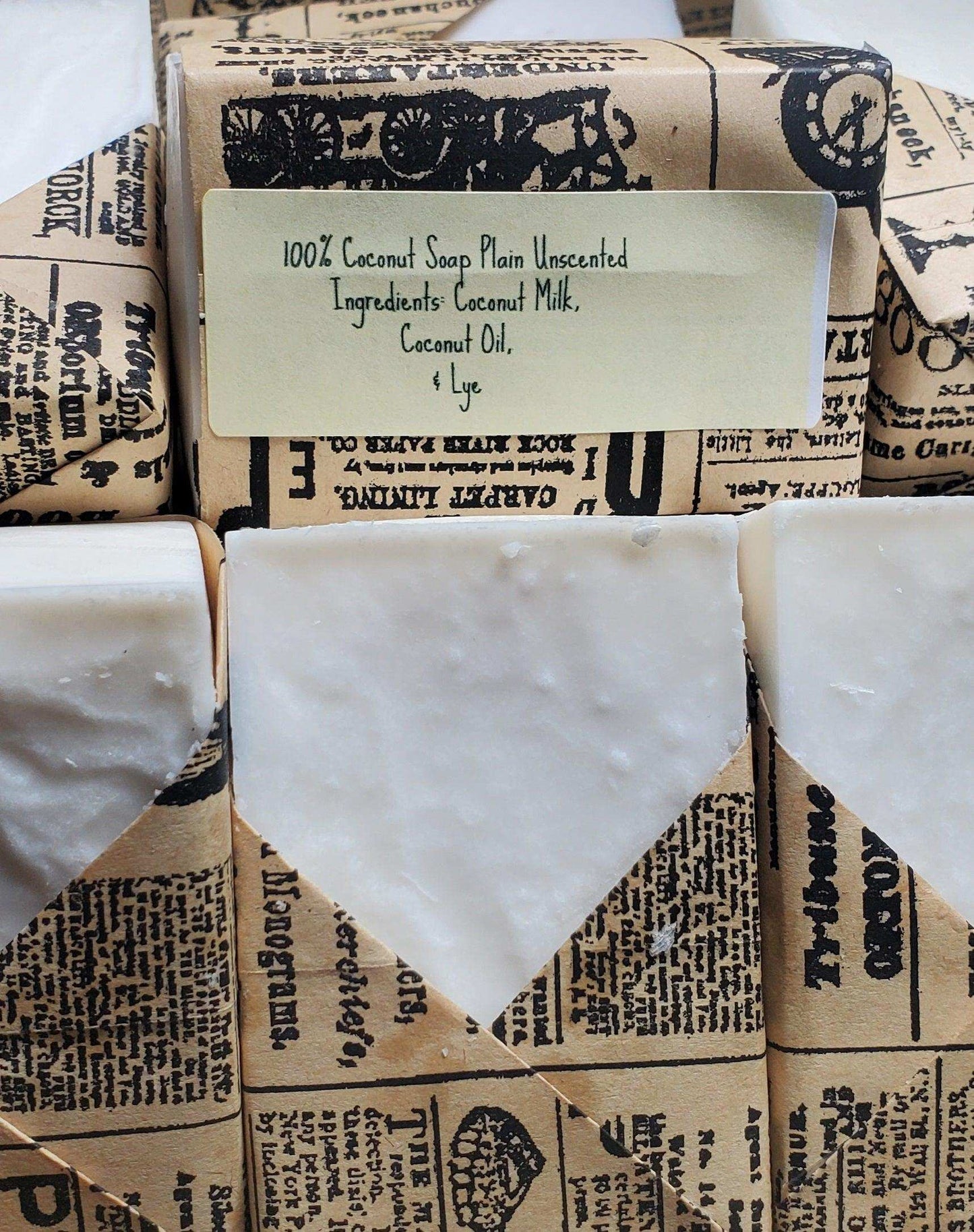 Rows of plain unscented coconut soap bars wrapped in rustic paper, labeled with natural ingredients like coconut milk and lye.