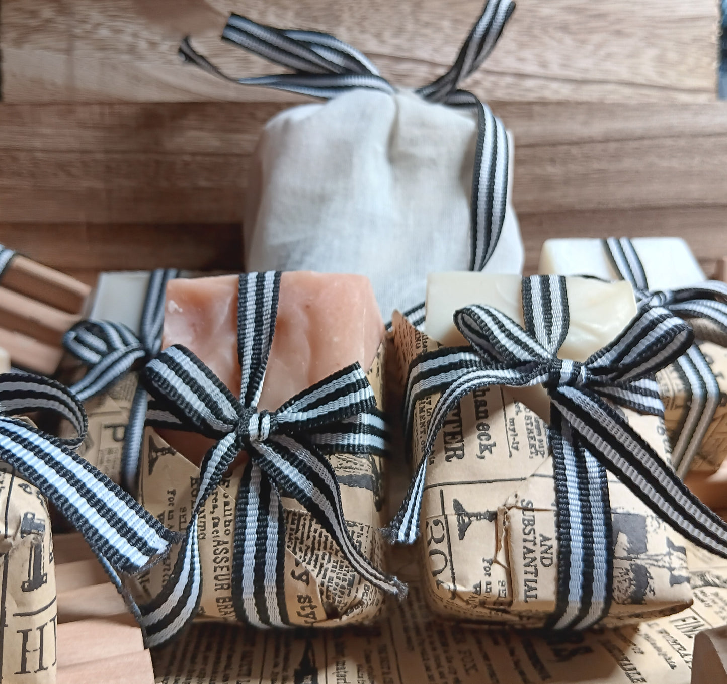 Three bars of goat milk soap wrapped in paper with ribbons on a wooden surface