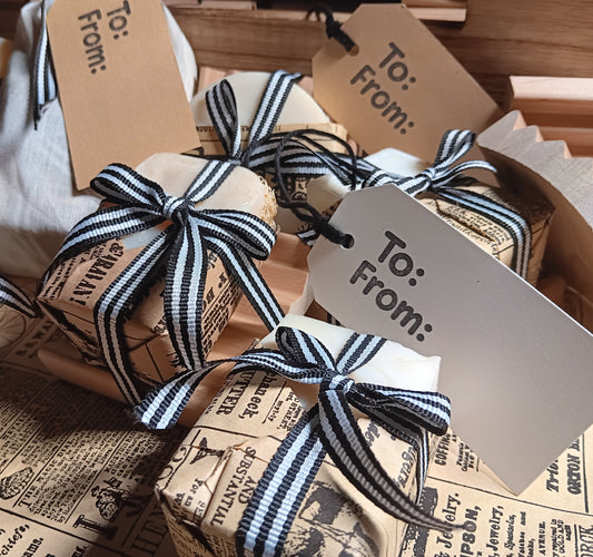 Gift soaps made with goat milk wrapped in brown paper with black and white striped ribbons and 'To: From:' tags.