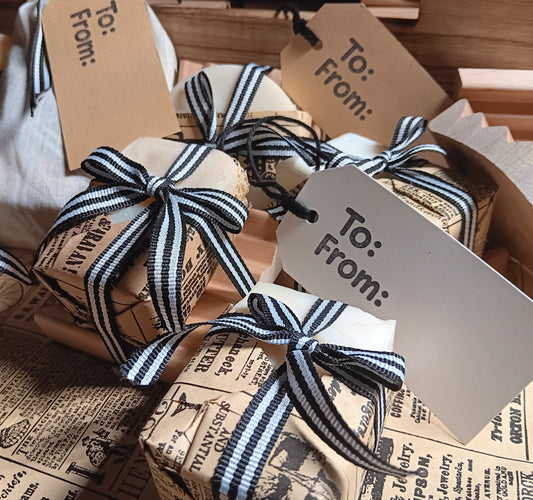 Gift soaps made with goat milk wrapped in brown paper with black and white striped ribbons and 'To: From:' tags.