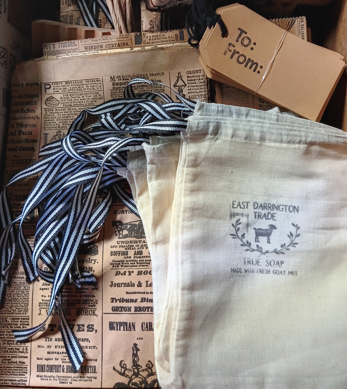 White drawstring bag with 'East Darrington Trade' branding on 2 types of newsprint bags. With To From Tags Wholesale Only 