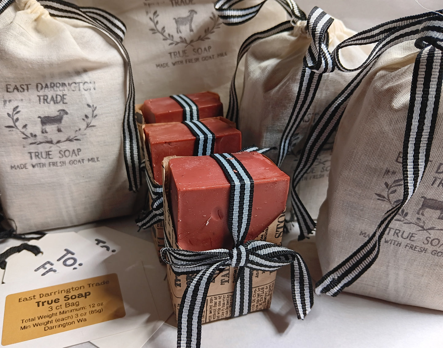 Morroccan red clay and spice cold processed soap bars tied with black and white ribbons on a white surface with branded bags in the background.  Wholesale Minimum order $100
