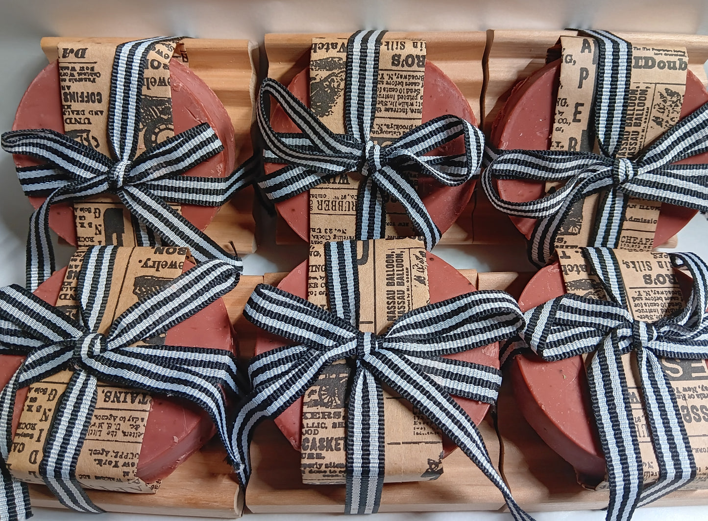 Red goat milk soap round bars with black and white striped ribbons on a wooden red alder soap dishes with newspaper print wrapping