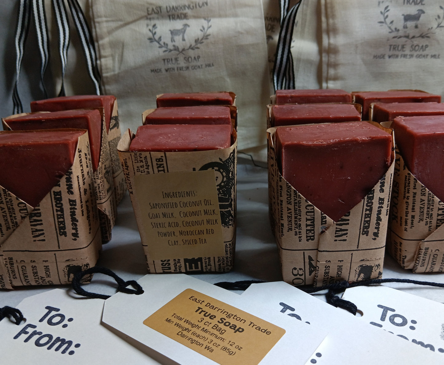 Morroccan Red Clay and Spice Soap bars in brown paper wrapper with 'True Soap' branding, surrounded by gift tags and packaging. Wholesale PreOrders 