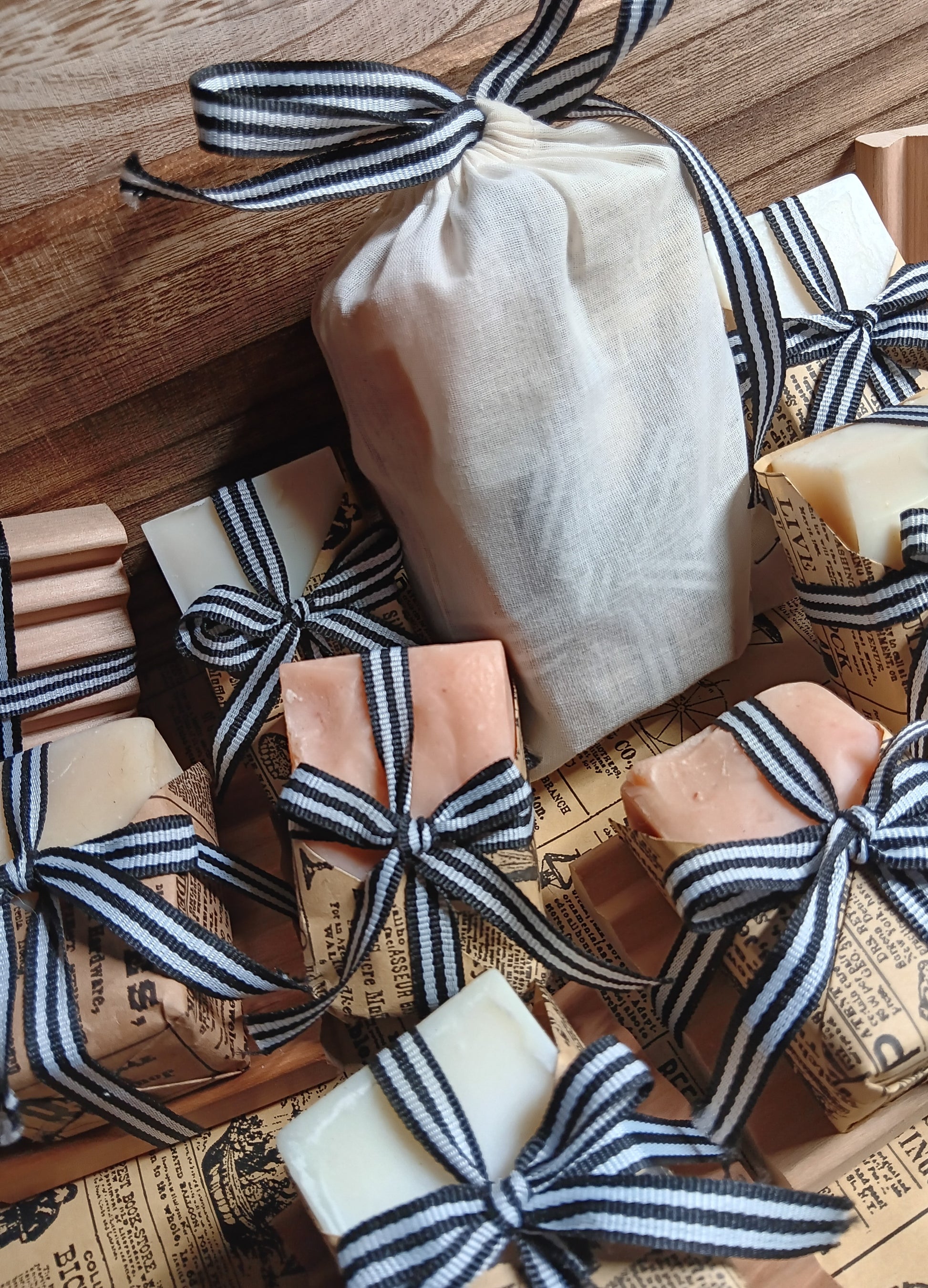 Handmade goat milk soaps wrapped in black and white ribbons on a wooden surface with newspaper background.