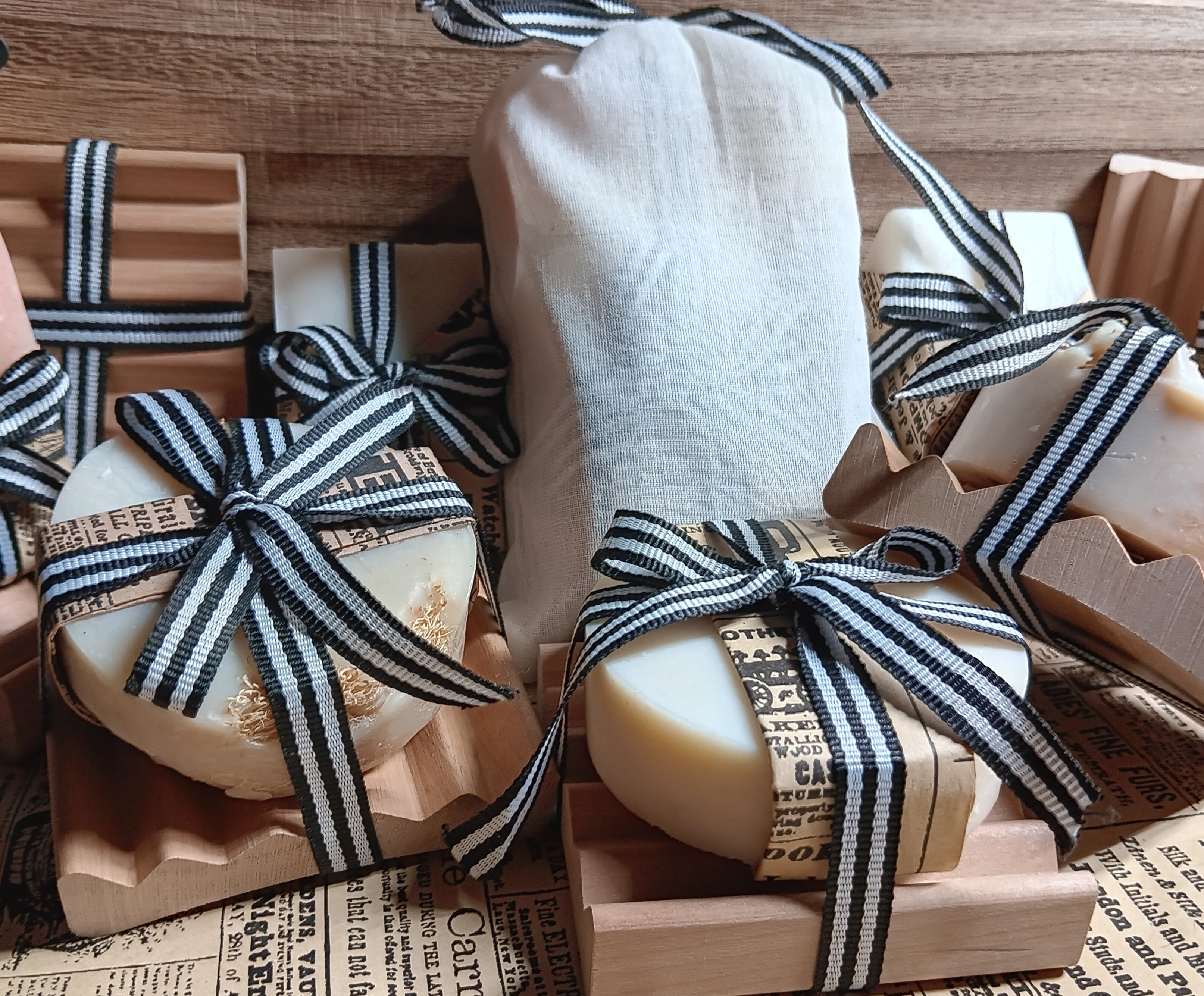 Bars of cold processed goat milk soaps wrapped in brown paper and black and white ribbons on a wooden surface.