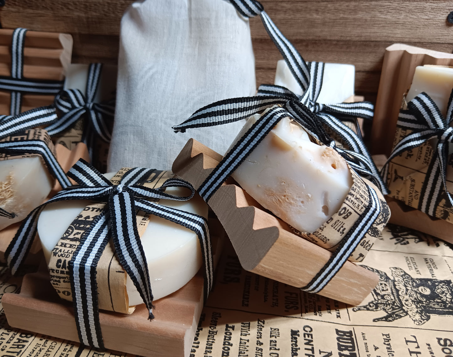 Bars of cold processed goat milk soaps with black and white striped ribbons on a wooden tray with newspaper background