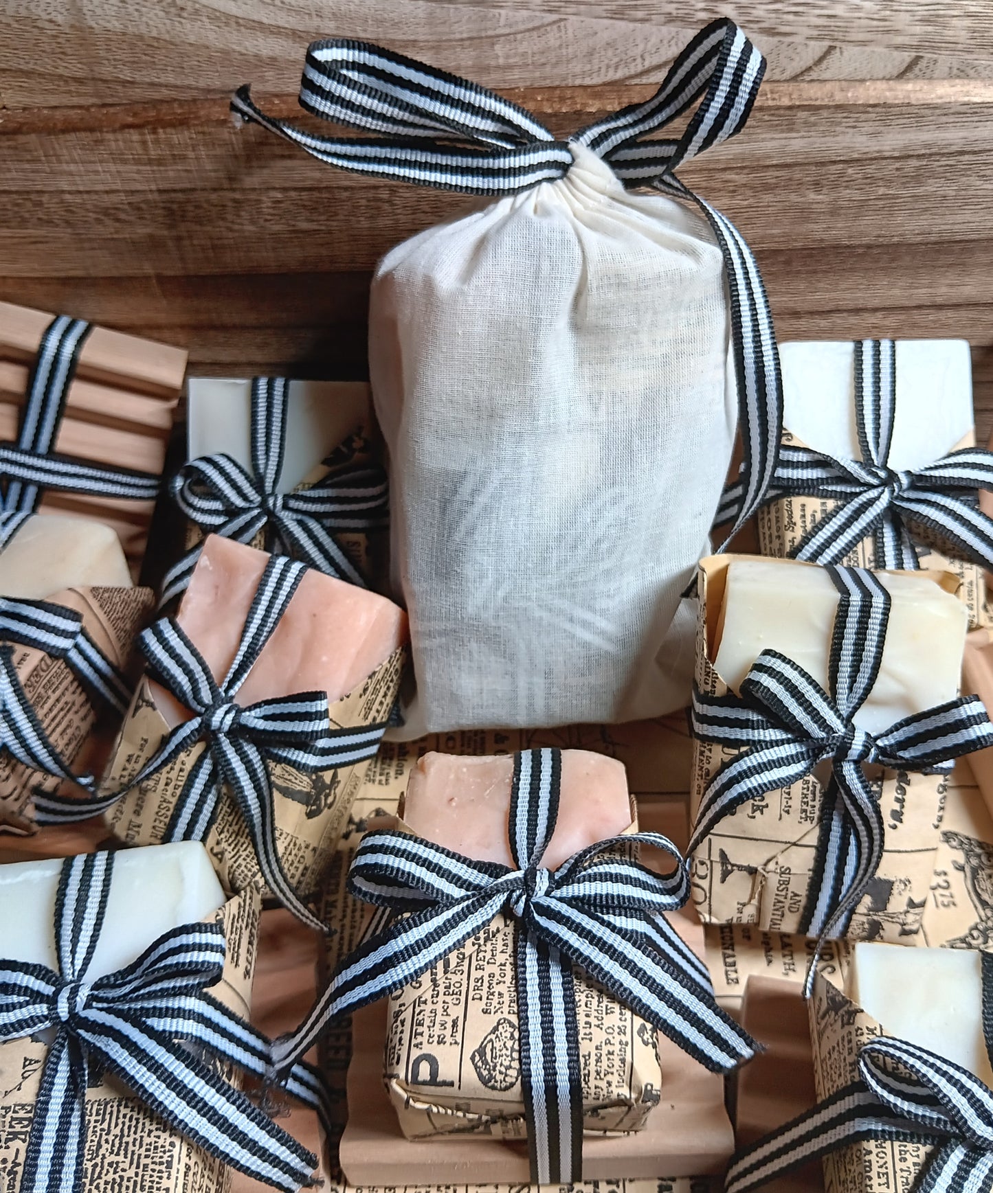 Handmade cold processed goat Milk soap bars wrapped in paper and tied with black and white ribbons on a wooden surface.