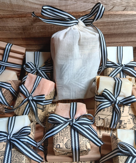 Handmade cold processed goat Milk soap bars wrapped in paper and tied with black and white ribbons on a wooden surface.