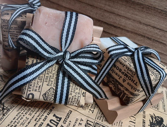 Goat milk soap bars with black and white striped ribbons on a wooden block, placed on vintage newspaper.