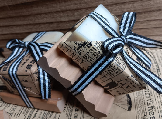 Bar of goat milk soap with a wooden handle wrapped in brown paper and a black and white striped ribbon on a wooden surface.