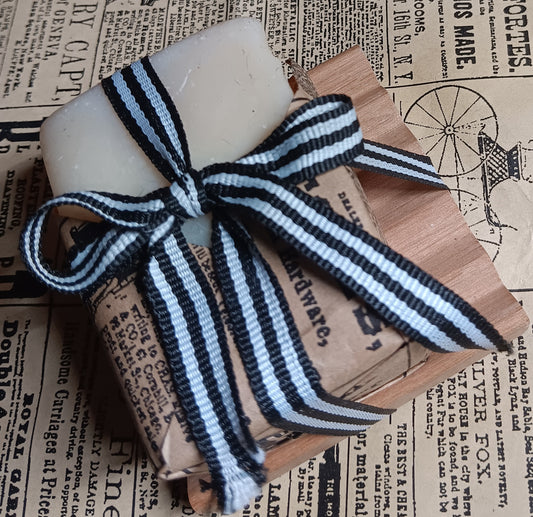 Bar of goat milk soap with a striped ribbon on a wooden block, placed on vintage newspaper.