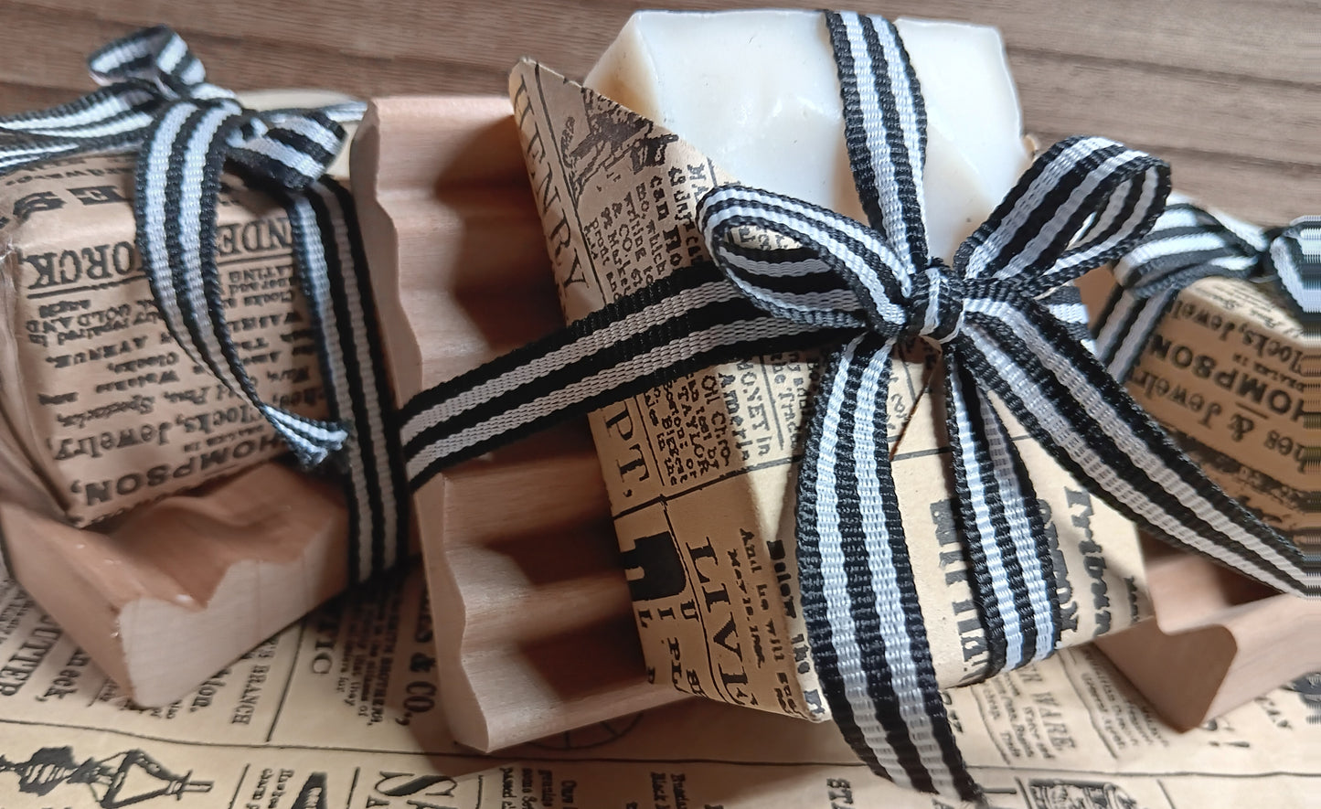 Three bars of goat milk soap wrapped in brown paper with black text and ribbons on a surface.