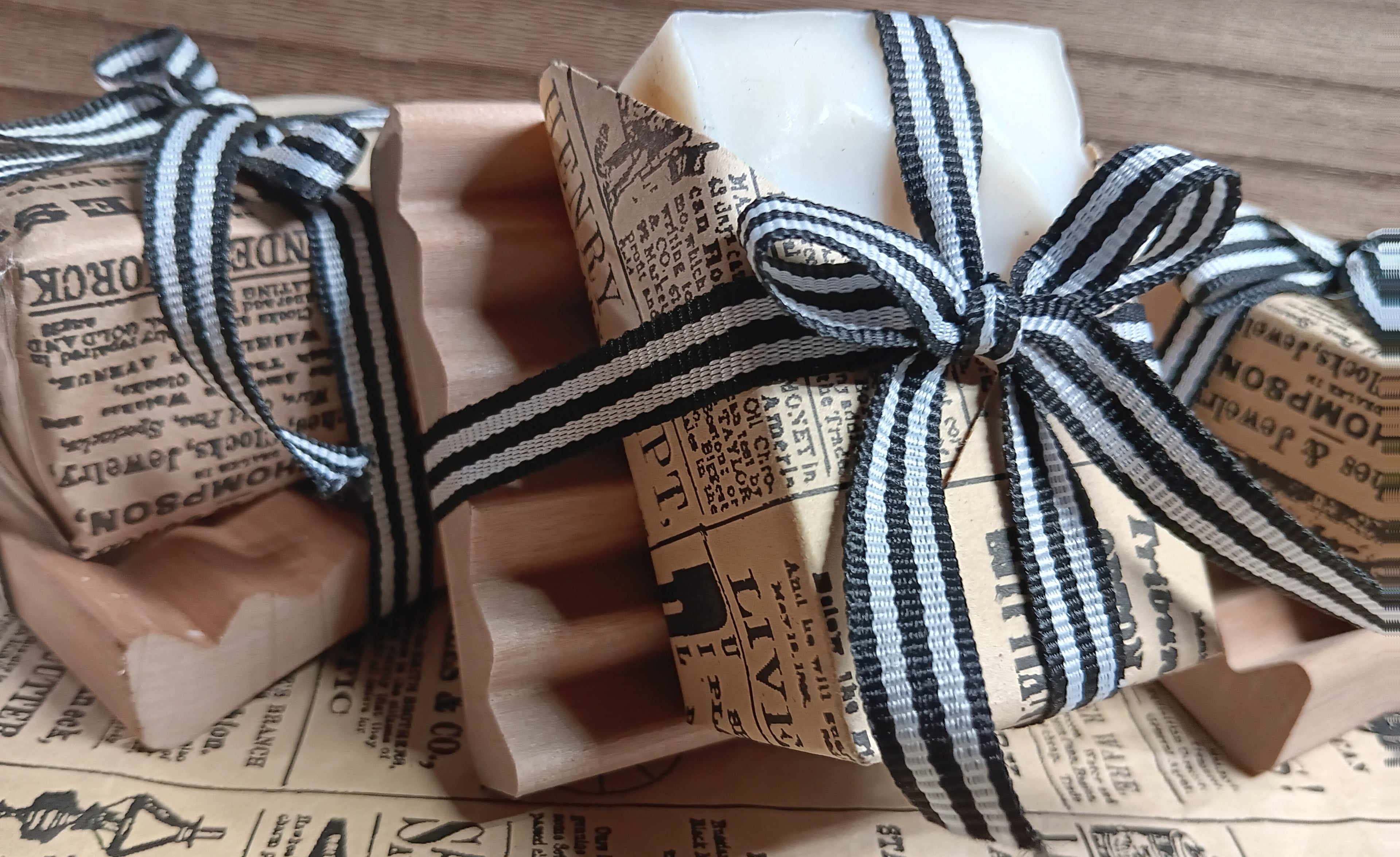 Three bars of goat milk soap wrapped in brown paper with black text and ribbons on a surface.