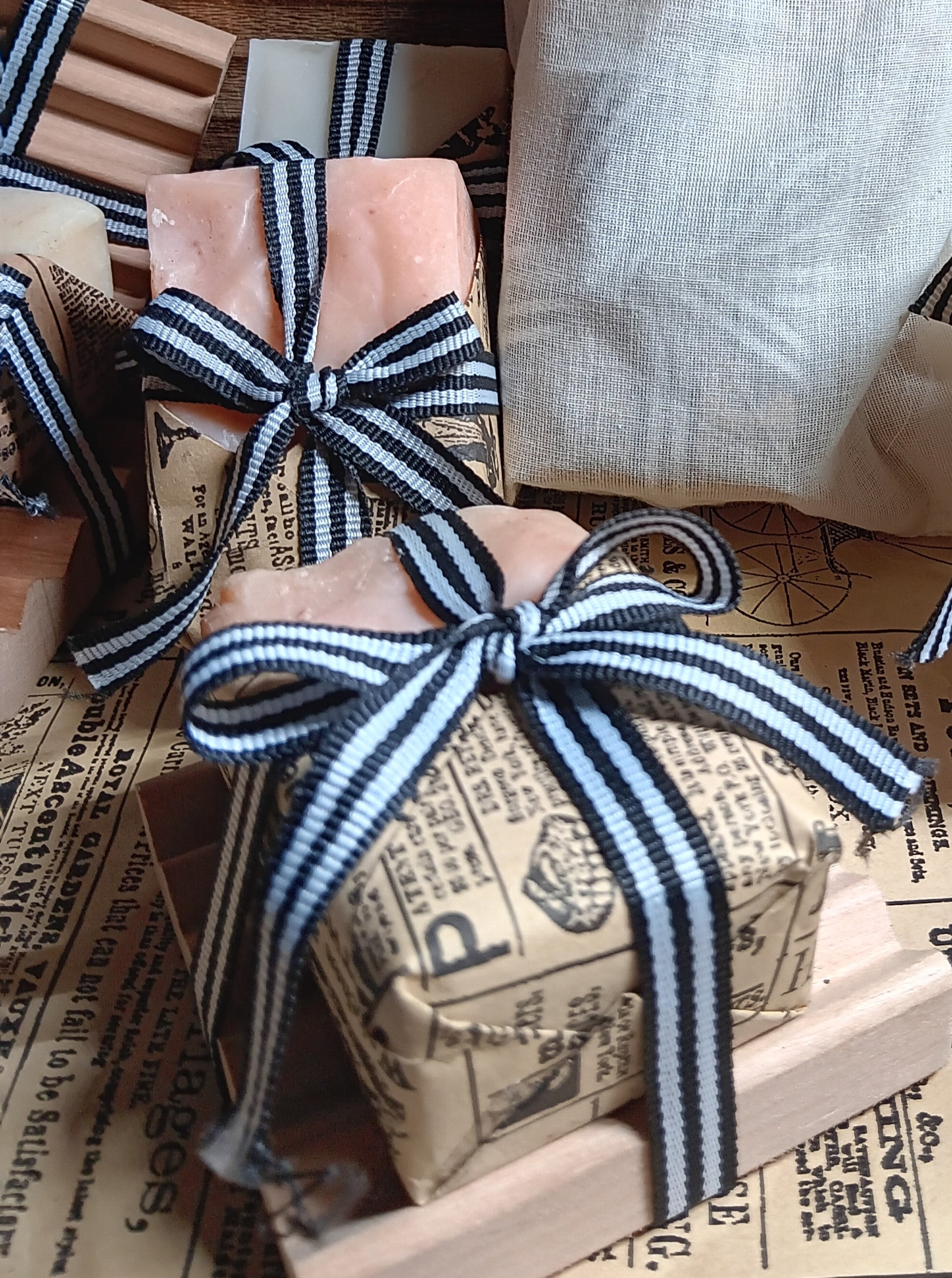 Gift boxes of goat milk soap wrapped with black striped ribbons on a newspaper background