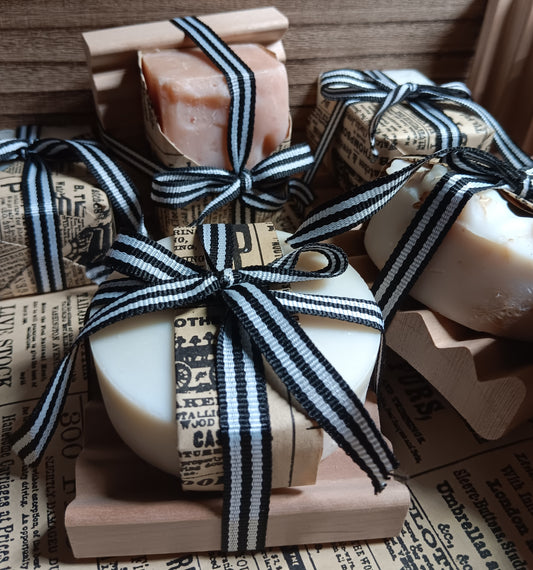 Round Bar of cold processed soap wrapped in black and white striped ribbon on a wooden block with newspaper background