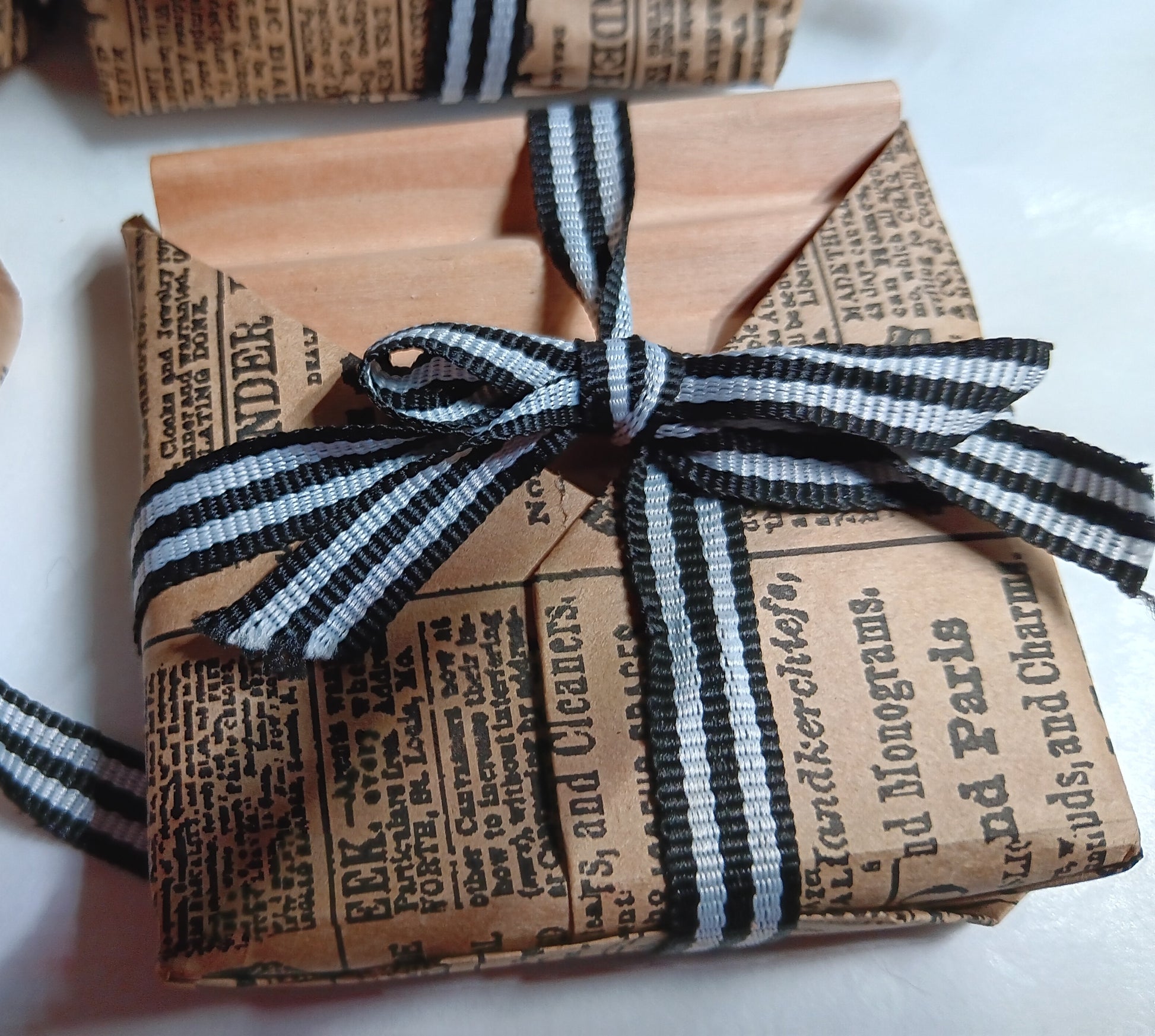 Gift wrapped soap dish in newspaper-style paper with a black and white striped ribbon.