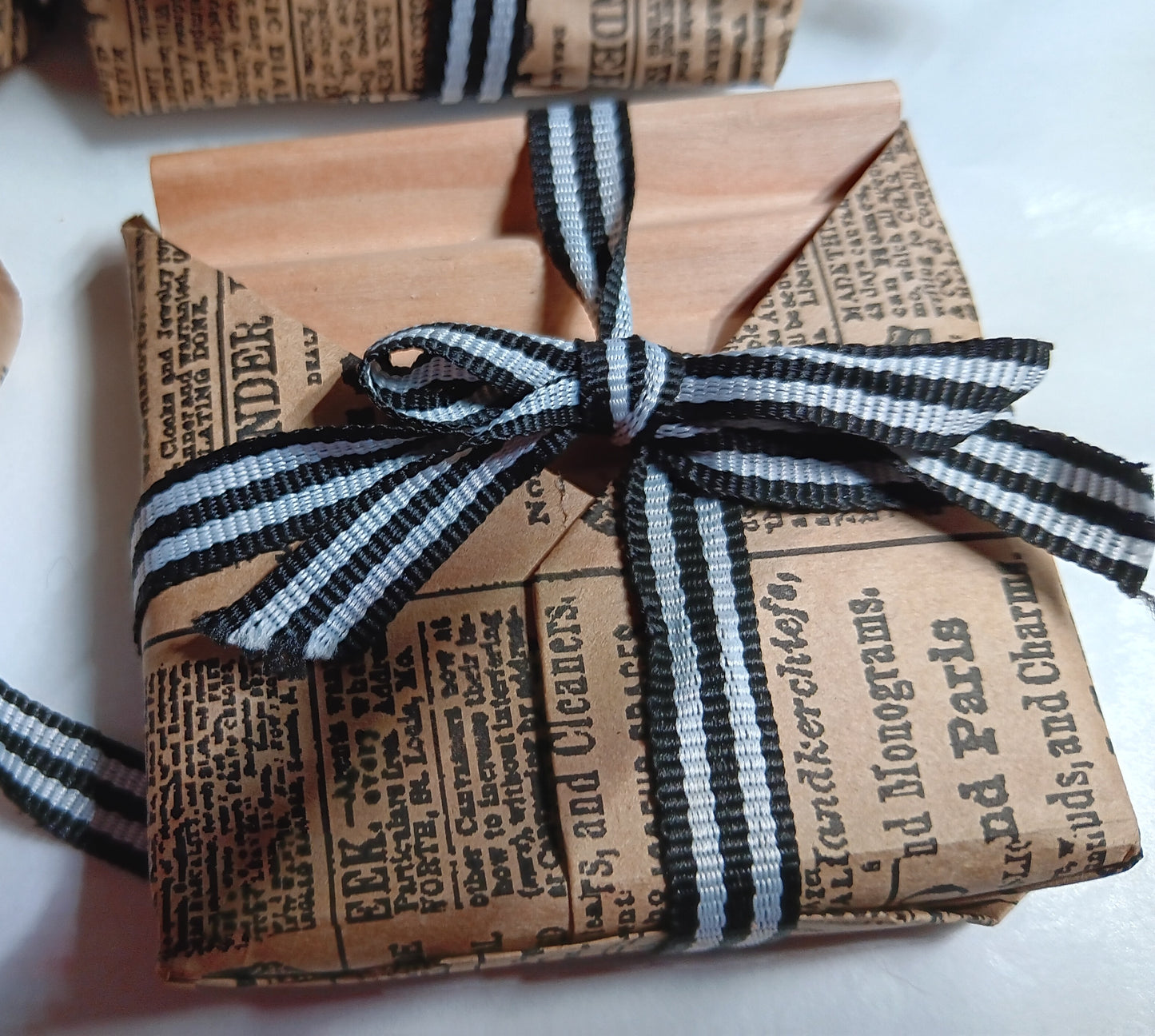 Gift wrapped soap dish in newspaper-style paper with a black and white striped ribbon.