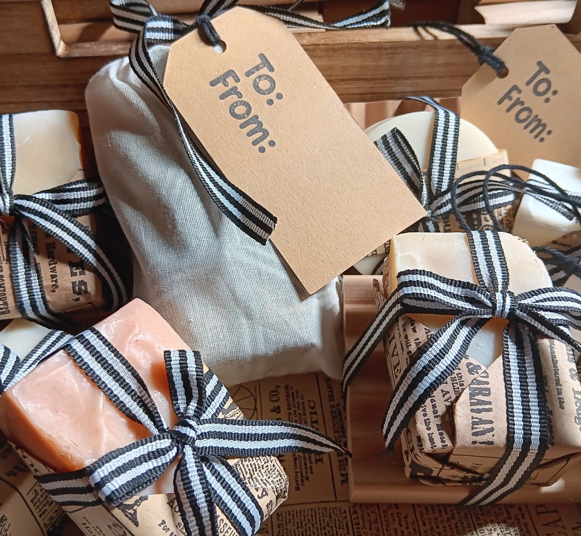 Handmade goat milk soap bars wrapped in newspaper and ribbon with 'To: From:' tags.